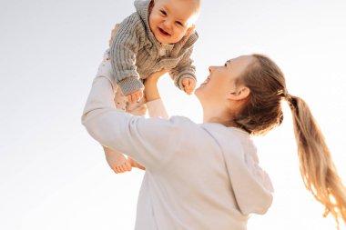 Genç ve güzel anne bebeğiyle dışarıda oynuyor. Mutlu ve sevgi dolu bir aile. Anne ve küçük oğlu anneler gününü kutlarken oynuyorlar ve sarılıyorlar.