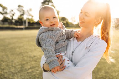 Anne ve çocuğun portresi, dışarıda çocuğunu kucaklayan gülen genç bir anne. Anne ve çocuğu baharın erken zamanlarının tadını çıkarıyorlar, anne ve küçük çocuk kucaklaşıyorlar, anneler gününü birlikte kutluyorlar.