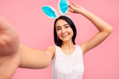 Tavşan kulaklı güzel, neşeli bir kadın stüdyoda pembe bir arka planda selfie çekiyor. Yüksek kalite fotoğraf