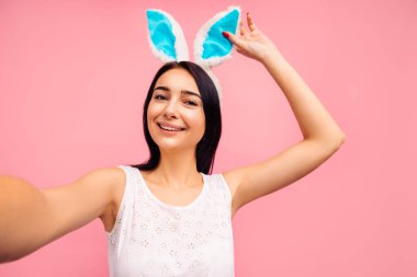 Tavşan kulaklı güzel, neşeli bir kadın stüdyoda pembe bir arka planda selfie çekiyor. Yüksek kalite fotoğraf