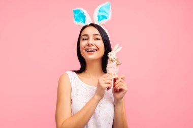 Tavşan kulaklı tatlı bir kadın elinde oyuncak bir tavşan tutuyor, geleneksel bir bayram, stüdyoda pembe bir arka planda, bir paskalya hediyesi. Yüksek kalite fotoğraf