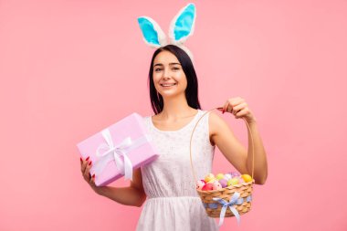 Tavşan kulaklı güzel bir kadın elinde bir sepet renkli yumurta, geleneksel bir tatil, stüdyoda pembe arka planda, Paskalya havasında.