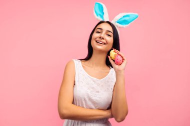 Tavşan kulaklı güzel ve pozitif bir esmer ve ellerinde boyalı Paskalya yumurtalarıyla, Paskalya