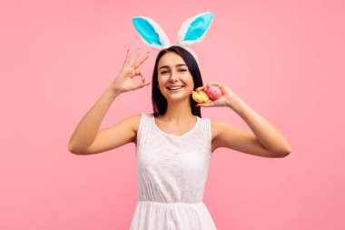 Tavşan kulaklı mutlu esmer kız ve boyalı paskalya yumurtaları stüdyoda pembe arka planda Paskalya jesti