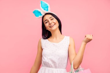 Tavşan kulaklı güzel bir kadın ellerinde alışveriş torbalarıyla, bahar alışverişi, geleneksel bir tatil, stüdyoda pembe arka planda, Paskalya havasında.