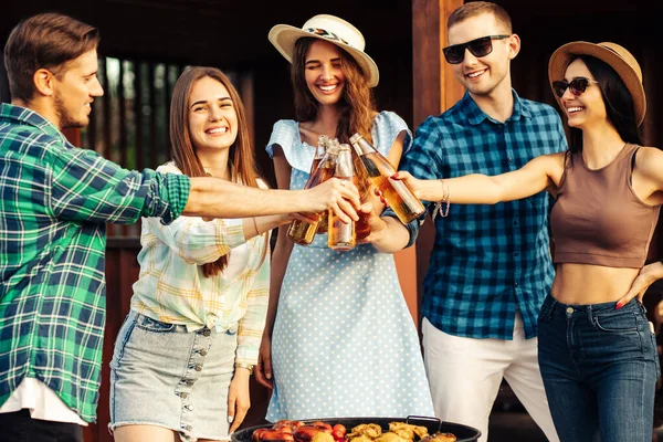 Four friends drink drinks, barbecue outdoors. Friends friends make a toast with their drinks at an open air party, enjoy outdoor recreation, celebrate meeting together
