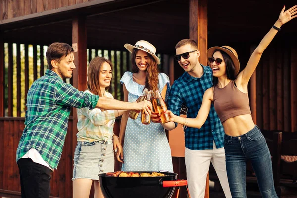 Four friends drink drinks, barbecue outdoors. Friends friends make a toast with their drinks at an open air party, enjoy outdoor recreation, celebrate meeting together
