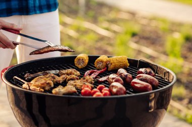 Adam arkadaşlar için barbekü hazırlıyor, mutlu genç arkadaşlar gün batımında dışarıda barbekü yapıyor, bir adam ızgarada et pişiriyor. Arkadaşlar barbekü partisinde eğleniyor.