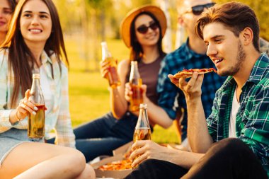 Bir grup arkadaş parkta pizzanın tadını çıkarıyorlar. Erkekler ve kadınlar pizza kutusunun etrafındaki çimlerde otururlar. Parkta piknik yapmak, doğada arkadaş olmak.