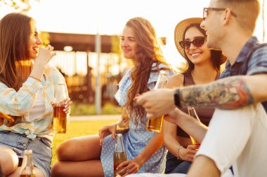 Bir grup arkadaş parkta pizzanın tadını çıkarıyorlar. Erkekler ve kadınlar pizza kutusunun etrafındaki çimlerde otururlar. Parkta piknik yapmak, doğada arkadaş olmak.