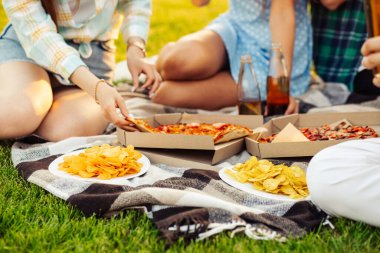 Bir grup arkadaş güneşli bir günde parkta piknik yapıyorlar. Bir grup arkadaş, bir bahar günü gün batımında, parkta yerde pizza yer, takılırız, eğleniriz.