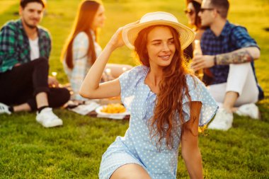 Bir grup arkadaş güneşli bir günde parkta piknik yapıyorlar. Bir grup arkadaş, bir bahar günü gün batımında, parkta yerde pizza yer, takılırız, eğleniriz.