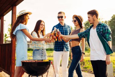Bir grup arkadaş doğada barbekü hazırlıyor - mutlu insanlar içkilerle piknikte eğleniyor. Bir grup mutlu arkadaş dışarıda barbekü yapıyorlar.
