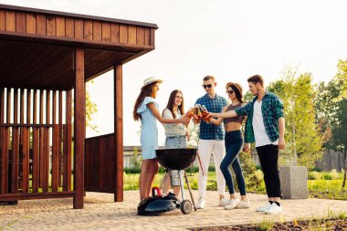 Bir grup arkadaş doğada barbekü hazırlıyor - mutlu insanlar içkilerle piknikte eğleniyor. Bir grup mutlu arkadaş dışarıda barbekü yapıyorlar.