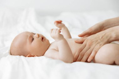 Smiling newborn baby on a white bed at home in a white sunny bedroom. Textiles and bed linen for children. Happy healthy baby concept, space for text