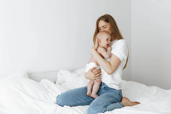 young caring mother hugged her little daughter, pressing her to her chest. Beautiful woman holding a newborn baby in her arms at home. Smiling mother hugging a small newborn baby showing love and care. motherhood concept, mother\'s day