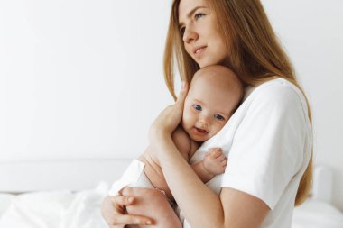 young caring mother hugged her little daughter, pressing her to her chest. Beautiful woman holding a newborn baby in her arms at home. Smiling mother hugging a small newborn baby showing love and care. motherhood concept, mother's day