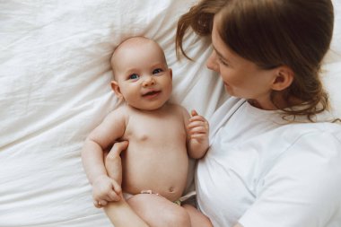 Portrait of a caring and loving mother kissing her little newborn daughter on the bed. beautiful mother playing with her little baby in the bedroom, top view. happy mother and child. Mother and child play and laugh. Happy family, mother's day