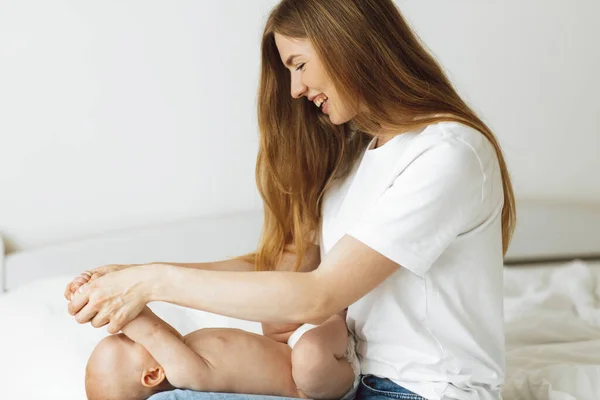 Happy baby in diaper gets belly massage from mother at home on white bed. Baby massage Mother massages her stomach, the child laughs. Treatment of colic. Massage and gymnastics for babies