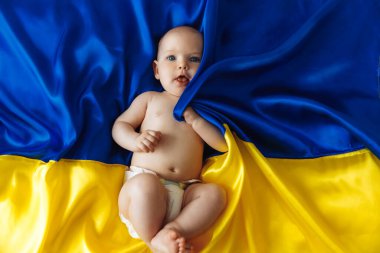 Pray for Ukraine.small defenseless baby lies on the Ukrainian Blue-yellow flag. protest against the war, Crisis, peace, end of aggression, child against the Russian war