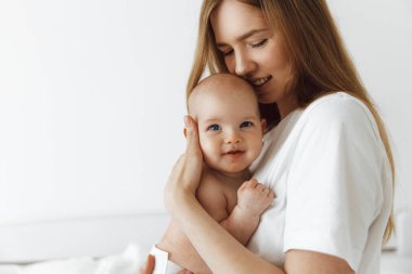 young caring mother hugged her little daughter, pressing her to her chest. Beautiful woman holding a newborn baby in her arms at home. Smiling mother hugging a small newborn baby showing love and care. motherhood concept, mother's day