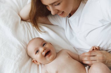 young mother with her little daughter, dressed in pajamas, relaxing in bed on the weekend and playing in bed together, lazy morning, warm and cozy scene. Pastel colors, top view.