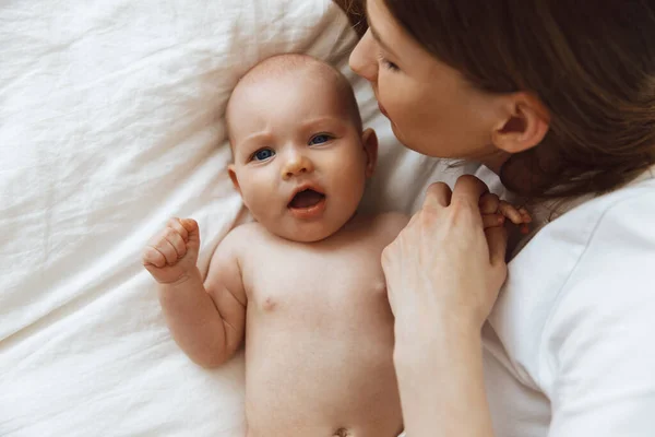 Portrait of a caring and loving mother kissing her little newborn daughter on the bed. beautiful mother playing with her little baby in the bedroom, top view. happy mother and child. Mother and child play and laugh. Happy family, mother\'s day