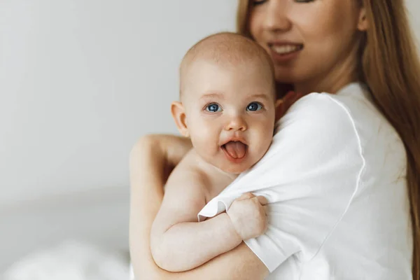 young caring mother hugged her little daughter, pressing her to her chest. Beautiful woman holding a newborn baby in her arms at home. Smiling mother hugging a small newborn baby showing love and care. motherhood concept, mother's day