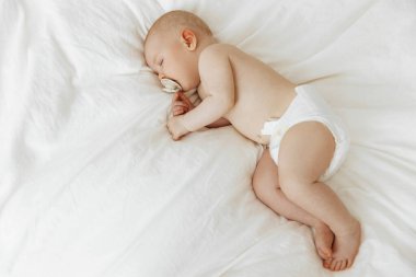 Beautiful little baby sleeps peacefully, lying on his side in bed indoors, relaxing during his daytime nap with his eyes closed. Toddler child napping indoors. Little girl sleeps at home on a white bed with her hand under her cheek