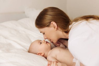 Portrait of a caring and loving mother kissing her little newborn daughter on the bed. beautiful mother playing with her little baby in the bedroom, top view. Happy family, mother's day