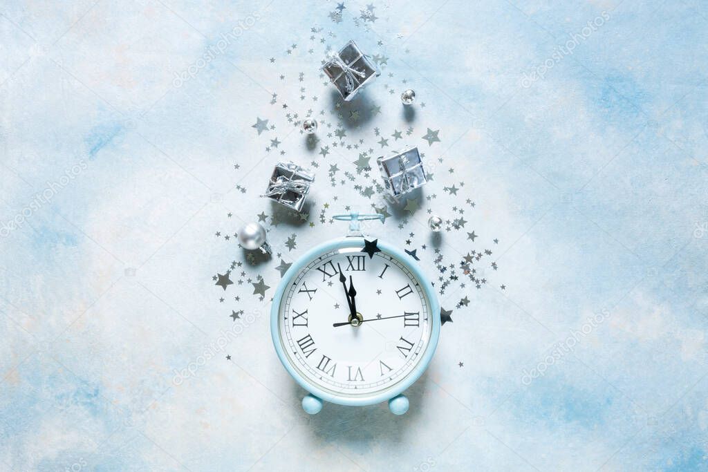 Christmas, New Year composition on sky blue background with modern alarm clock and silver color Christmas decorations - stars, confetti, balls and gift boxes, top view, flat lay
