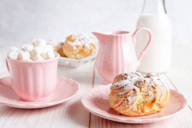 Taze kremalı çörekler, pembe bardakta sıcak içecek ve beyaz arka planda şekerleme. Günaydın aşk konsepti.