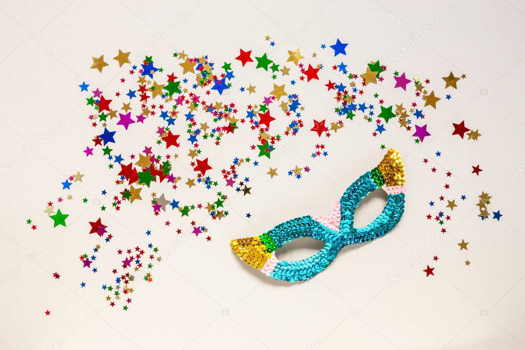 Carnival mask and varicolored glitter confetti. Top view, Close up on light cream background	