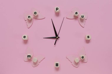 Alarm clock hands and word menopause on the pink background with butterflies. clipart