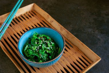 Bambu tepsisinde yemek çubuklarıyla kase içinde su yosunu.