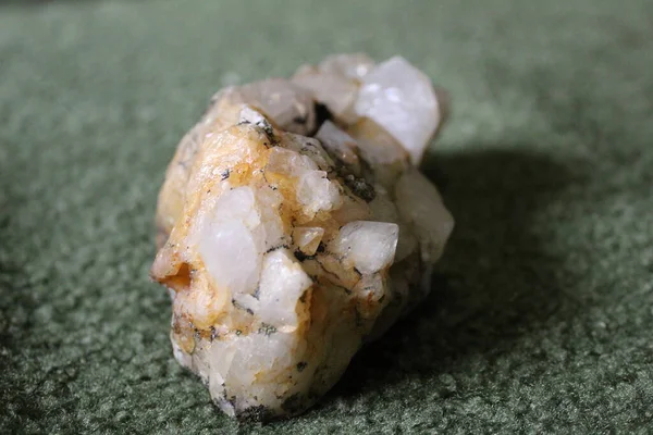 close-up of natural unprocessed rock crystal on a green background / photo of a beautiful unprocessed stone.large natural rhinestone. white, transparent color. inclusions of yellow and black.