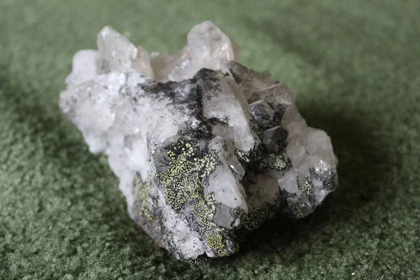 close-up of natural unprocessed rock crystal on a green background / photo of a beautiful unprocessed stone.large natural rhinestone. white, transparent color. inclusions of yellow and black.