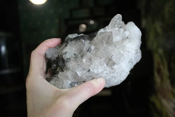 close-up of natural unprocessed rock crystal in a woman\'s hand / photo of a beautiful unprocessed stone. a woman holds a crystal in her hand. large natural rhinestone. white, transparent color. inclusions of yellow and black.