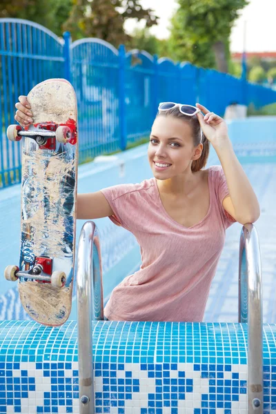 A beautiful young girl with a scateboard on the pool ladder — Stock Photo, Image