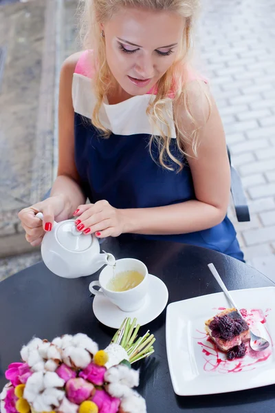 Krásná mladá blondýnka v létě šaty u stolu v pav — Stock fotografie