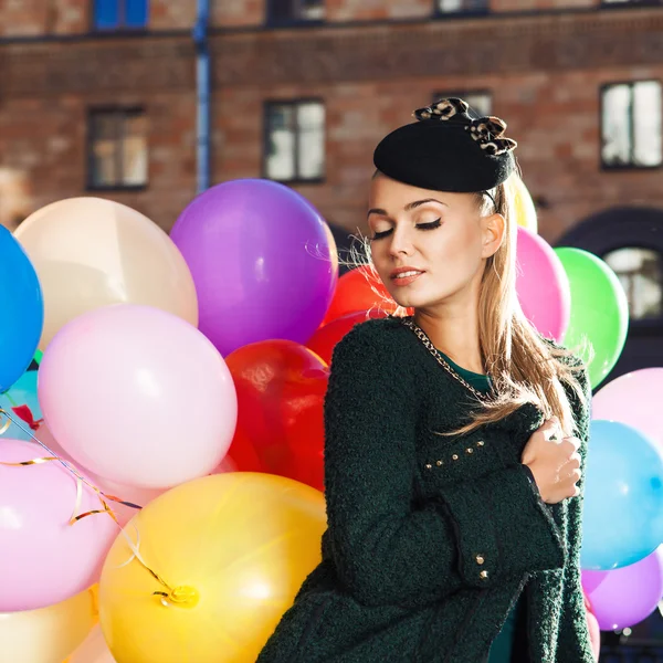 Beautiful lady in retro outfit holding a bunch of balloons in ci — Stock Photo, Image