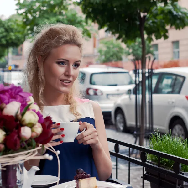 Krásná mladá blondýnka v létě šaty u stolu v pav — Stock fotografie