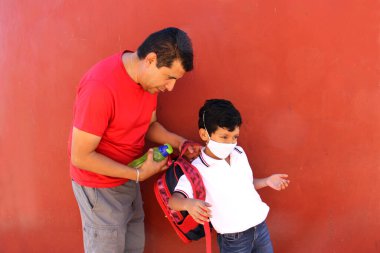 Latin baba ve oğlu, Covid-19 salgınından dolayı okula dönmek için yüz maskeleri ve sırt çantalarıyla hazırlanıyorlar.