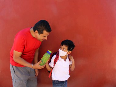 Latin baba ve oğlu, Covid-19 salgınından dolayı okula dönmek için yüz maskeleri ve sırt çantalarıyla hazırlanıyorlar.