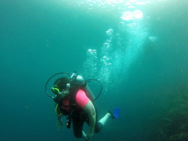 Kadın oksijen tüpüyle suyun derinliklerine dalıyor. Gözlükler mutlu ve heyecanlı bir deneyim yaşıyor.