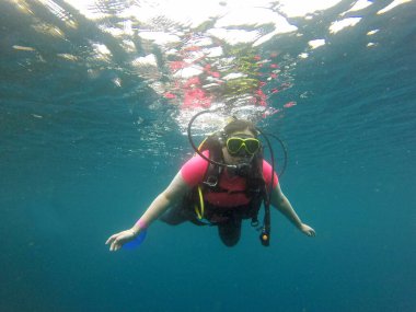 Kadın oksijen tüpüyle suyun derinliklerine dalıyor. Gözlükler mutlu ve heyecanlı bir deneyim yaşıyor.