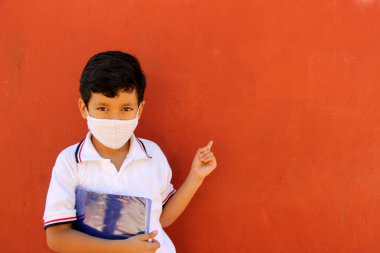 Üniformalı, maskeli, sırt çantalı, defterli ve su dolu Latin çocuk Coronavirus salgınından dolayı okula geri döndü.