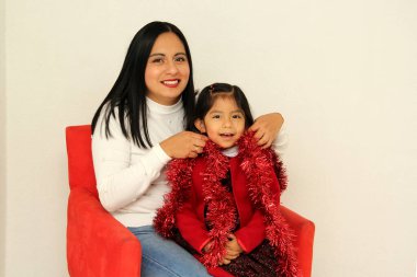 Gözlüklü, şapkalı ve Noel çelenkli Latin anne ve kızı Aralık 'ın gelmesiyle ilgili coşkularını ve mutluluklarını gösteriyorlar ve Noel ve yeni yılı kutluyorlar.