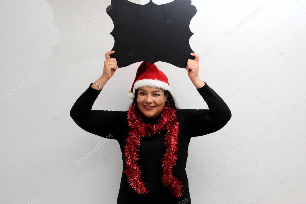 Latin adult woman with hat and Christmas garland shows banner and blank notebook to put a message of congratulations, love or wish list