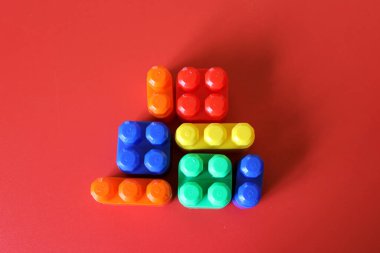 Pieces of plastic rainbow multicolored buildable toy blocks formed and arranged on red background